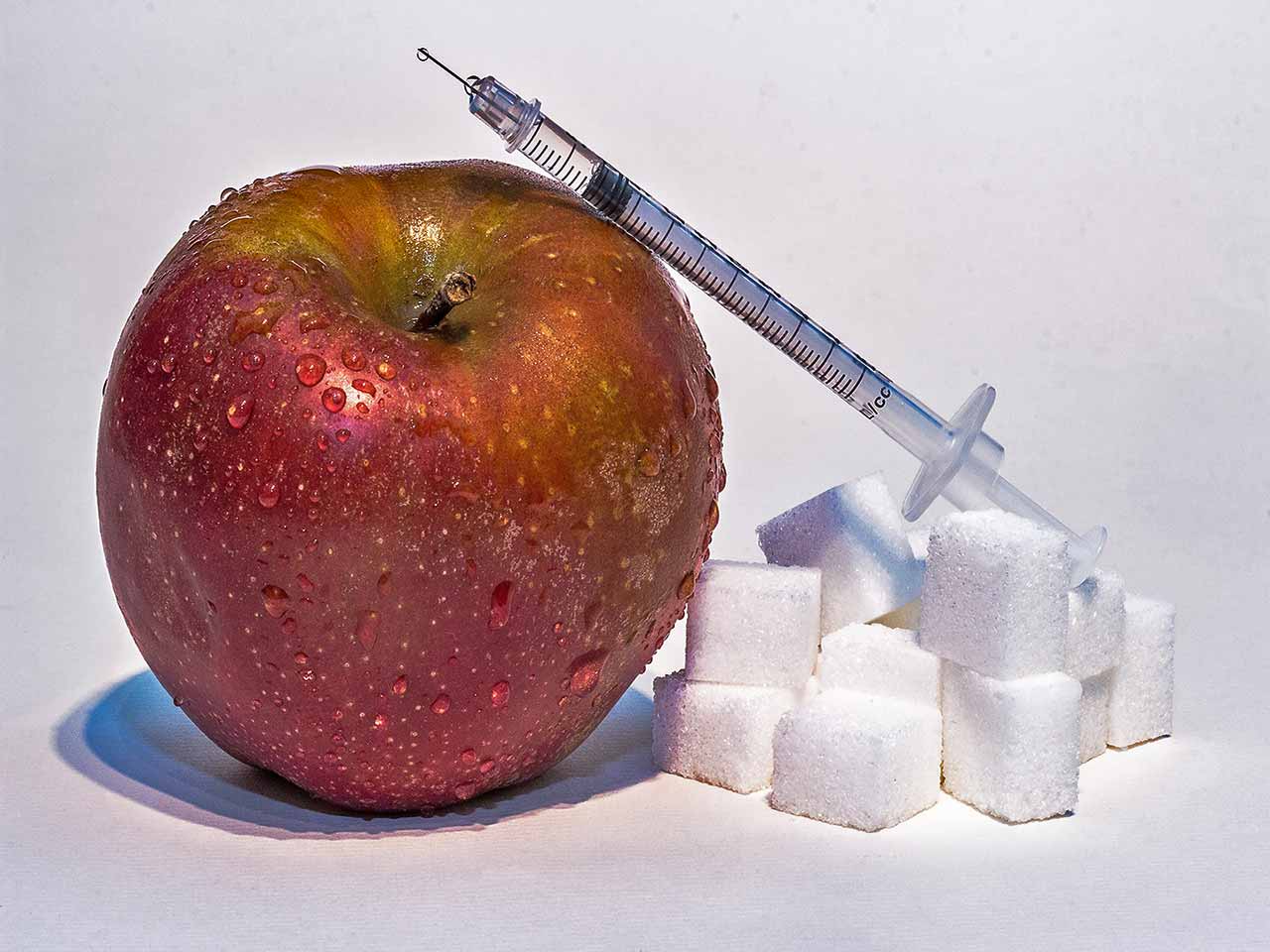 Il fruttosio, lo zucchero più nocivo: zollette di zucchero, frutta e una siringa di insulina